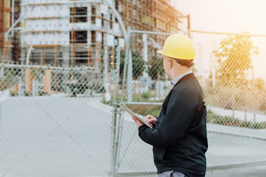 A construction worker holding a tablet in front of a construction site.