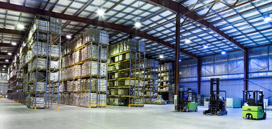 Interior of a large warehouse with tall shelves stacked with pallets and boxes, and three forklifts parked on the concrete floor. Interior of a large warehouse with tall shelves stacked with pallets and boxes, and three forklifts parked on the concrete floor.